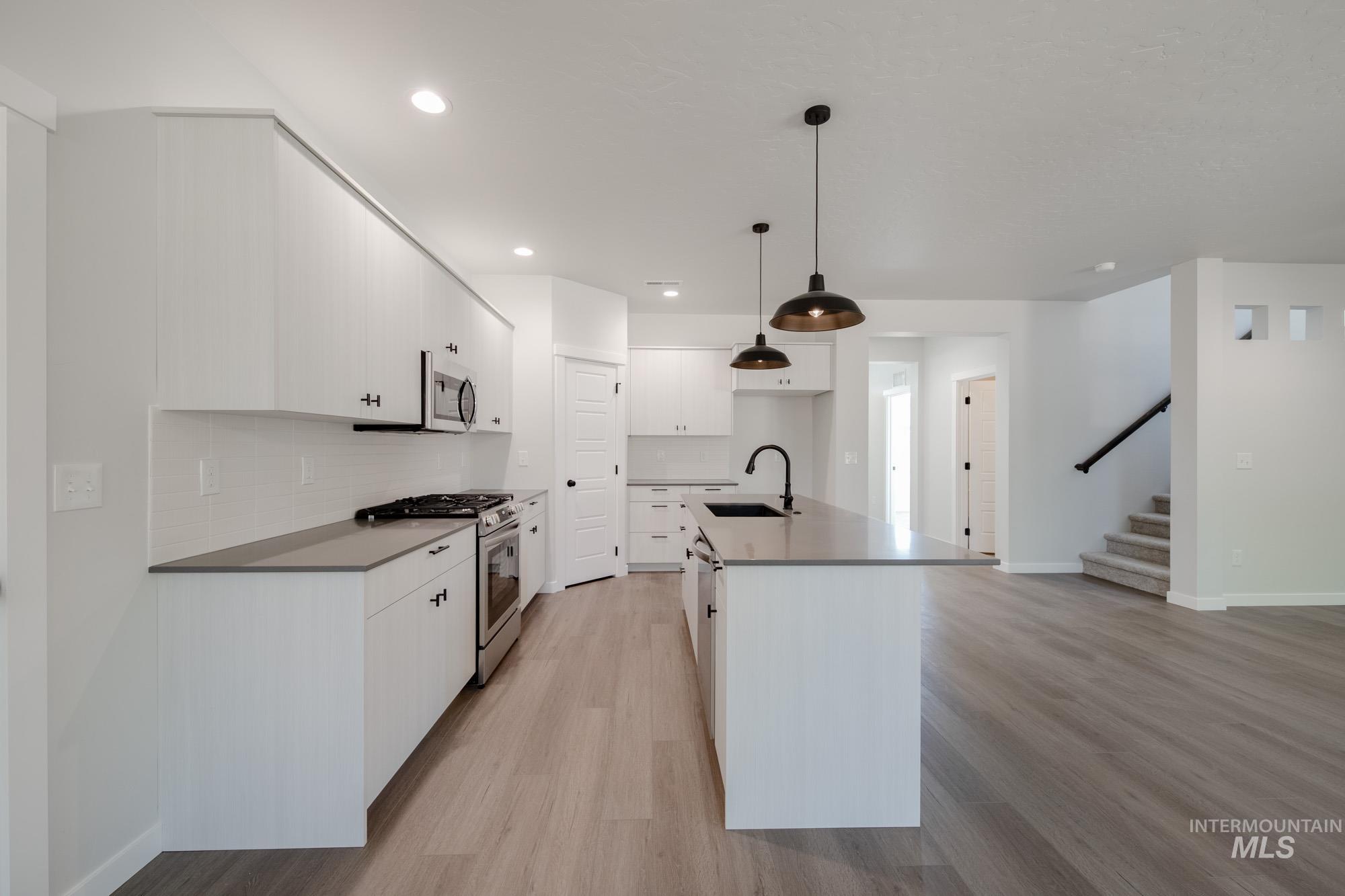 Kitchen with gas range oven, stainless steel microwave, light wood finished floors, tasteful backsplash, and white cabinets