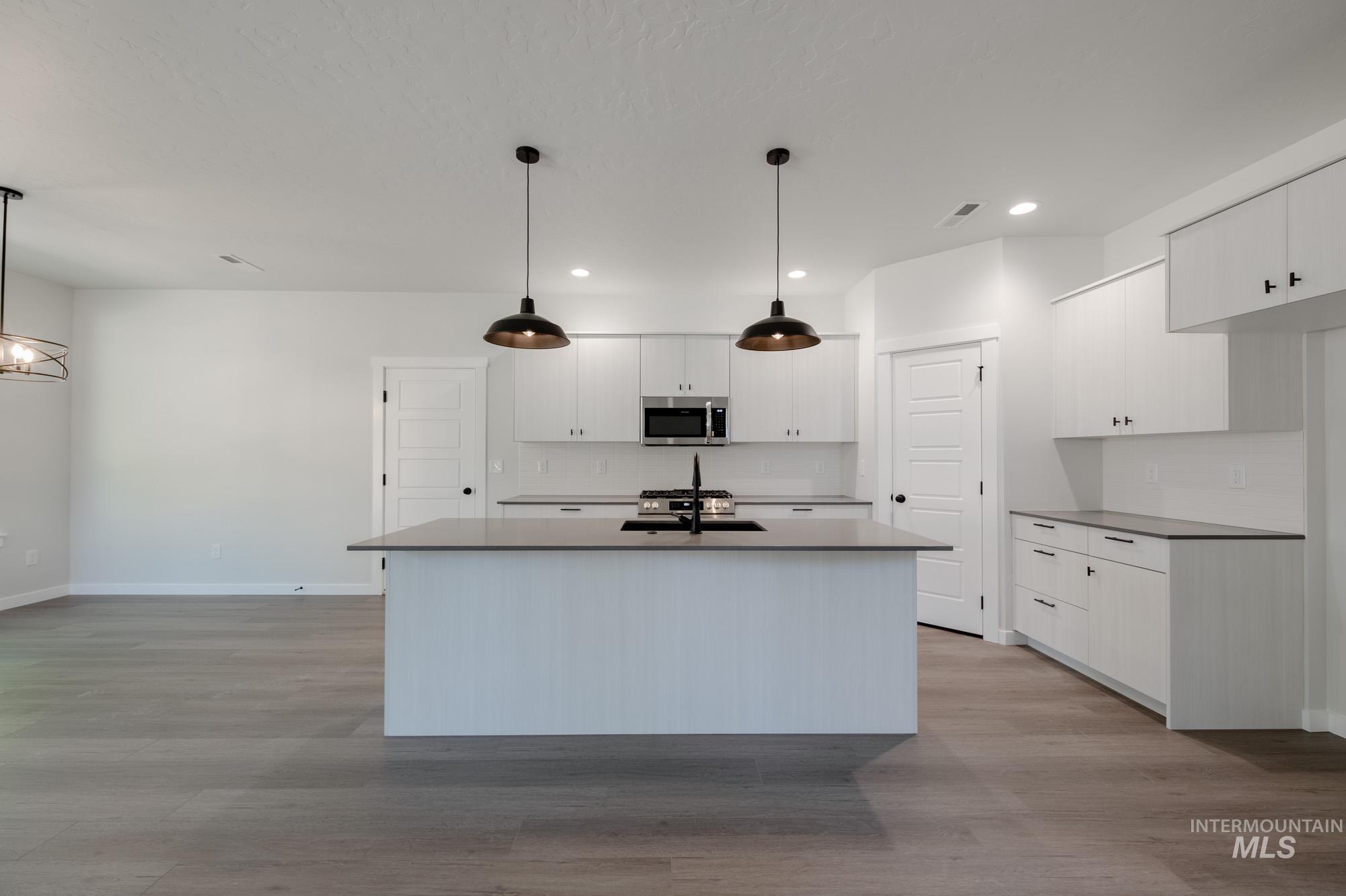Kitchen featuring stainless steel microwave, recessed lighting, light wood-type flooring, white cabinets, and an island with sink