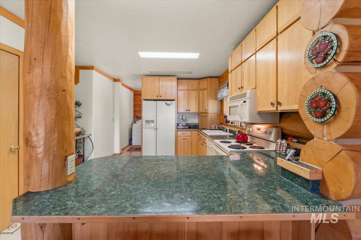 Kitchen featuring white appliances, light brown cabinetry, dark countertops, a peninsula, and washer / clothes dryer