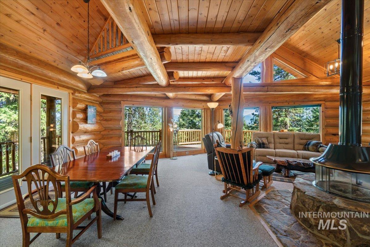 Dining area with a wood stove, healthy amount of natural light, carpet flooring, log walls, and high vaulted ceiling