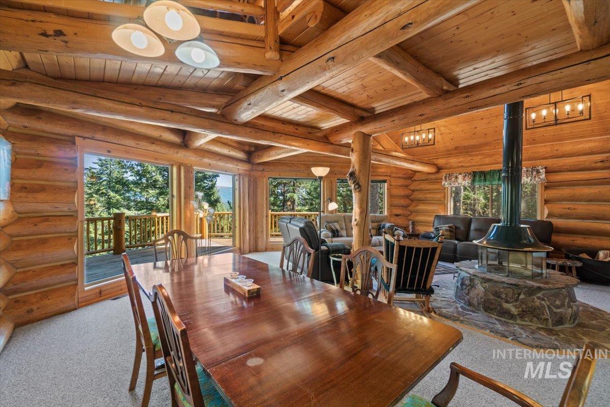 Carpeted dining space with rustic walls, a wood stove, and a wooden ceiling with exposed beams