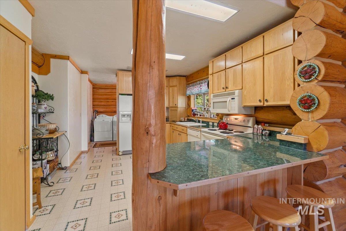 Kitchen with light brown cabinets, white appliances, light flooring, and a peninsula