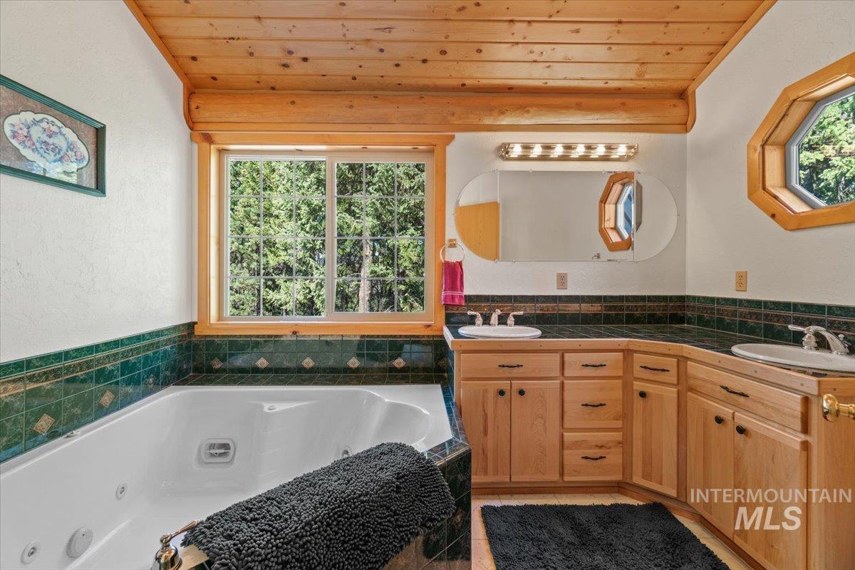 Bathroom featuring double vanity, a whirlpool tub, wooden ceiling, and a textured wall