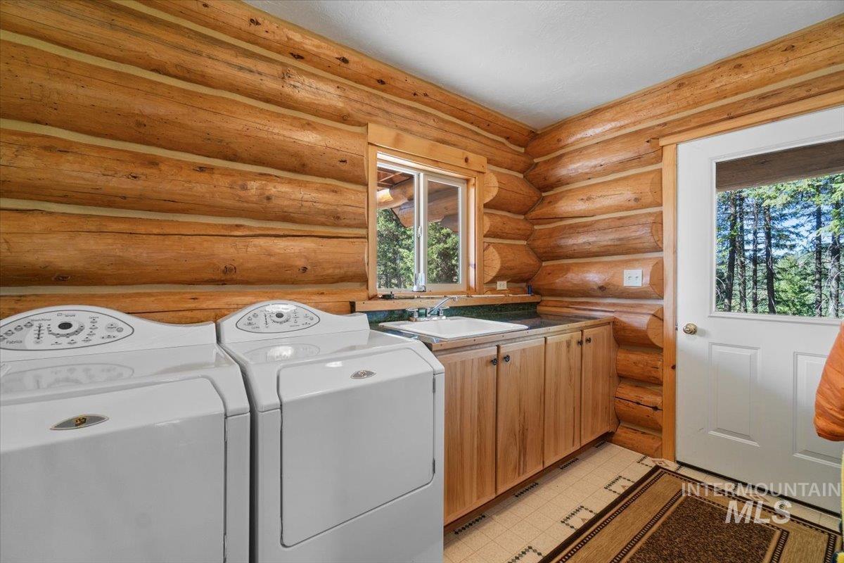 Laundry area with independent washer and dryer, log walls, and cabinet space