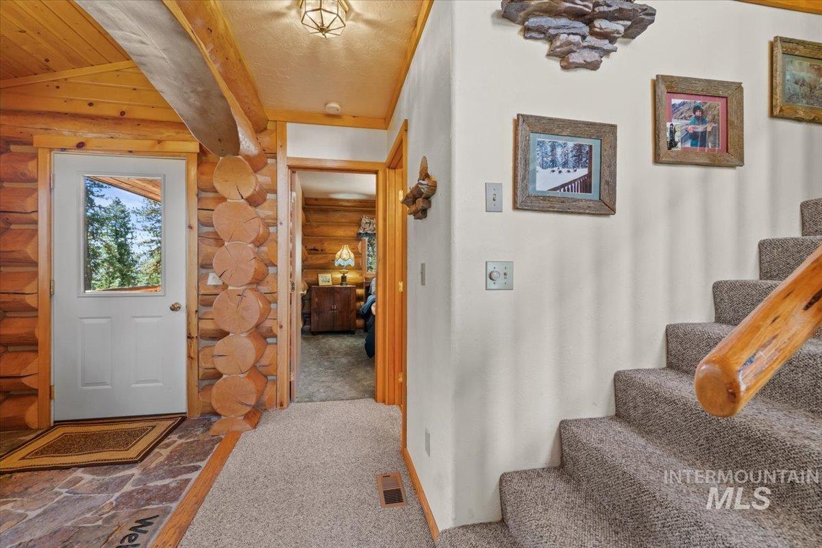 Entryway with stairway, carpet floors, log walls, beamed ceiling, and a textured ceiling