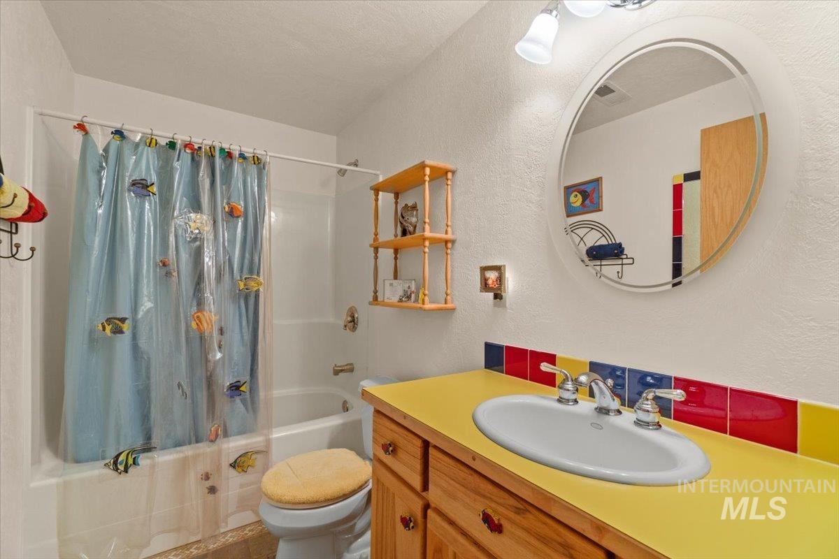Full bath with shower / bathtub combination with curtain, a textured wall, and vanity