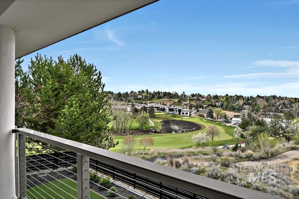 Balcony featuring a modern cable railing system, overlooking a manicured golf course, surrounding green spaces, and distant residential structures