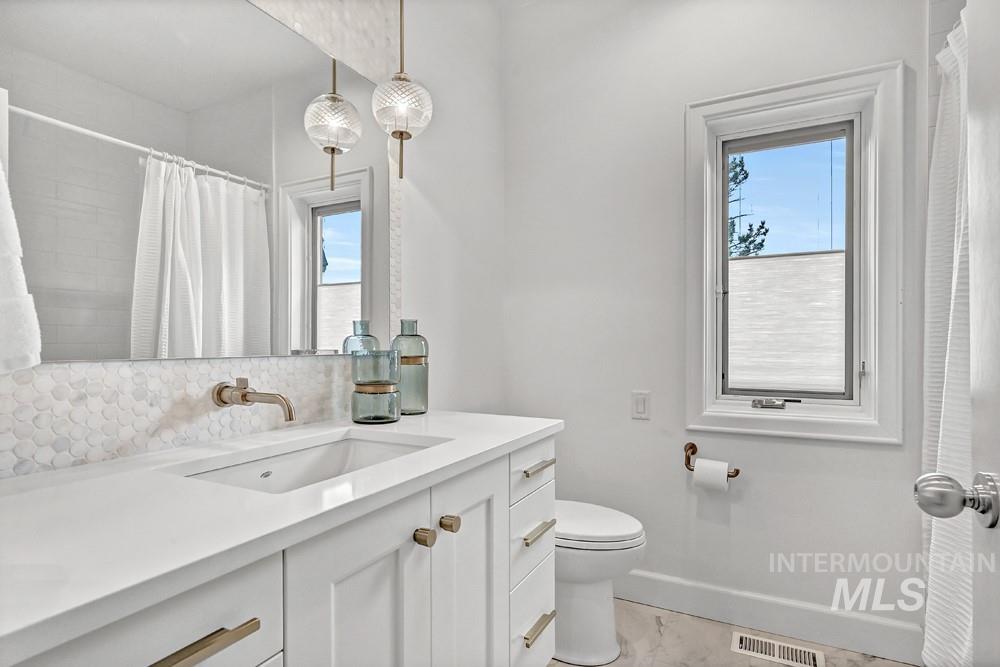 Bathroom featuring a white vanity with a rectangular undermount sink, a wall-mounted faucet, and two decorative pendant lights