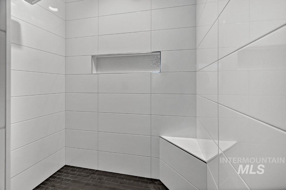 Tiled shower enclosure featuring white rectangular wall tiles, a dark-toned mosaic floor, an integrated shower niche, a built-in corner bench, and a wall-mounted shower head