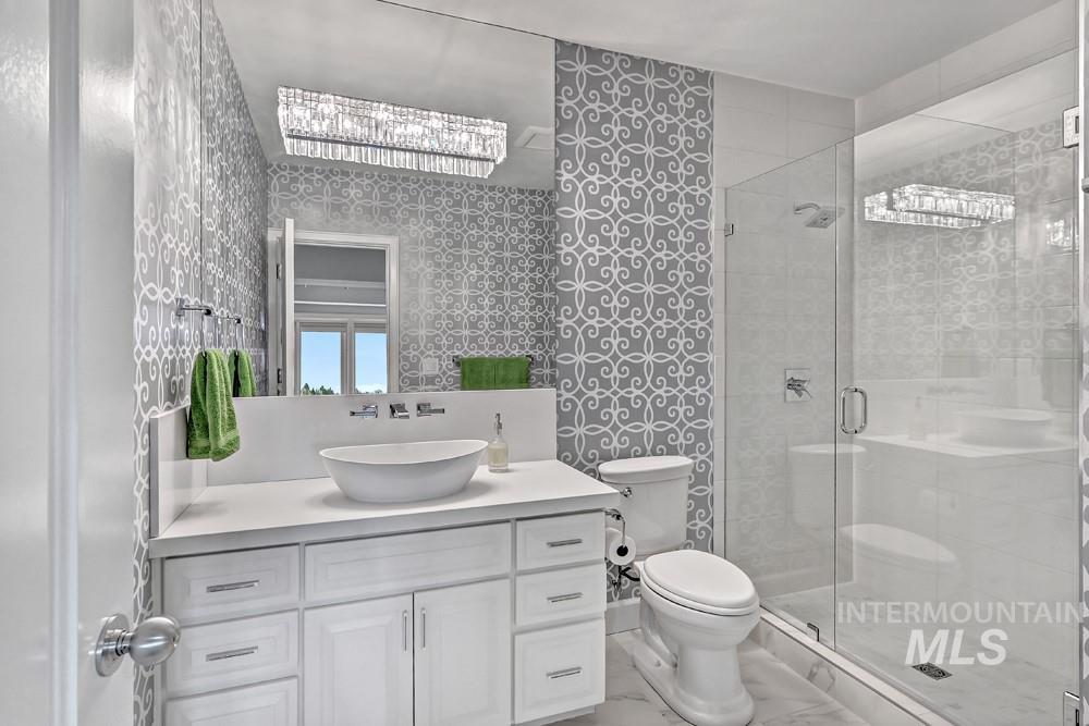 Bathroom featuring a glass-enclosed shower, white vessel sink, and a vanity with white cabinetry and chrome hardware