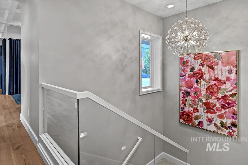 Staircase featuring a glass panel railing with white trim, wood-finish flooring, a contemporary chandelier, and a rectangular window