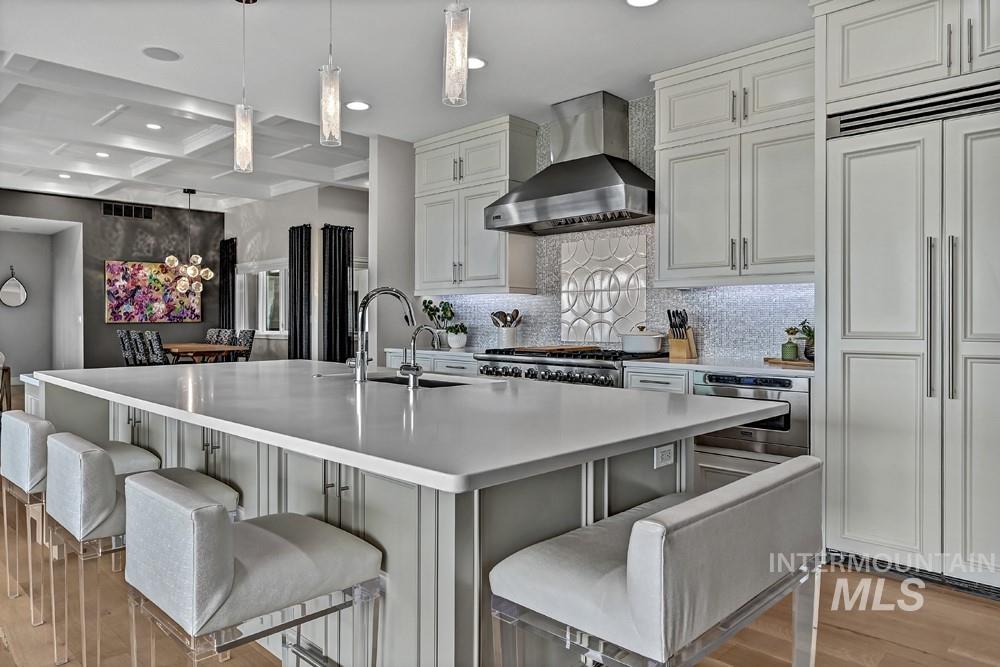 Expansive kitchen island with a light-toned countertop, wood-finish flooring, white cabinetry, integrated refrigerator, and a coffered ceiling