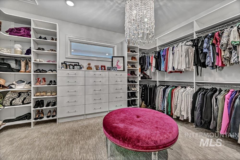 Custom walk-in closet featuring extensive built-in shelving, multiple hanging rods, integrated drawer storage, a horizontal window, and a prominent crystal chandelier