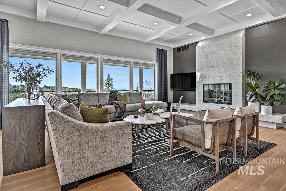 Spacious living area featuring a coffered ceiling, large picture windows, a full-height stone fireplace, and wood-finish flooring