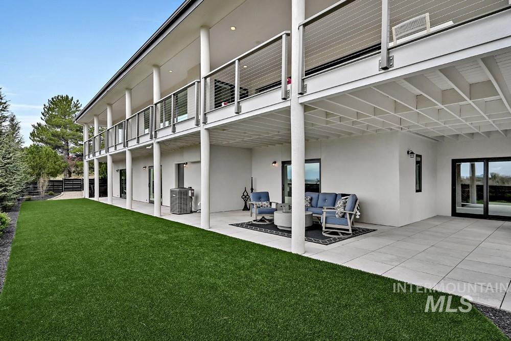 Expansive outdoor living area featuring a ground-level patio, a covered upper-level balcony with cable railings, and a low-maintenance artificial turf lawn