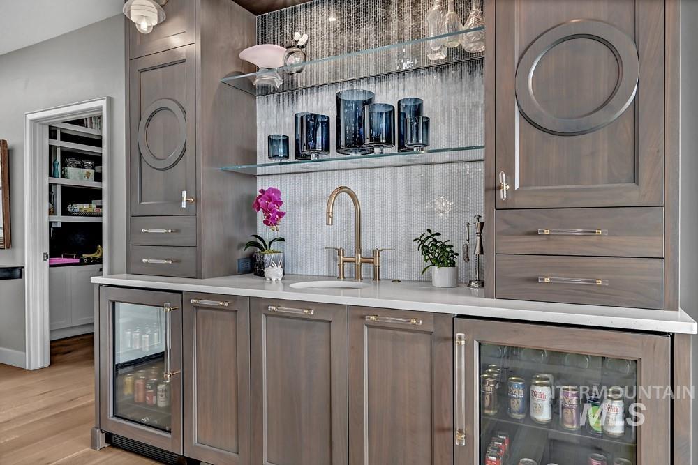 Built-in wet bar featuring custom wood cabinetry, a white countertop, and a circular basin with a gold-finish faucet