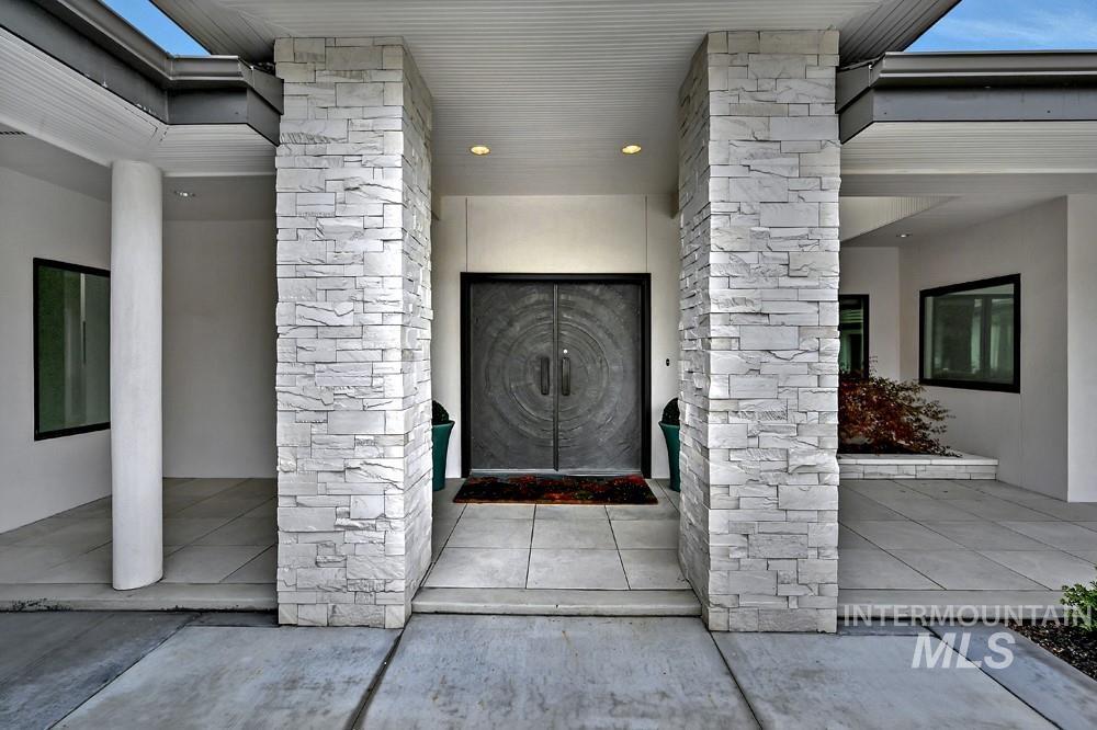 Modern entry with stacked stone columns, a double front door featuring circular detailing, concrete pathways, and recessed lighting
