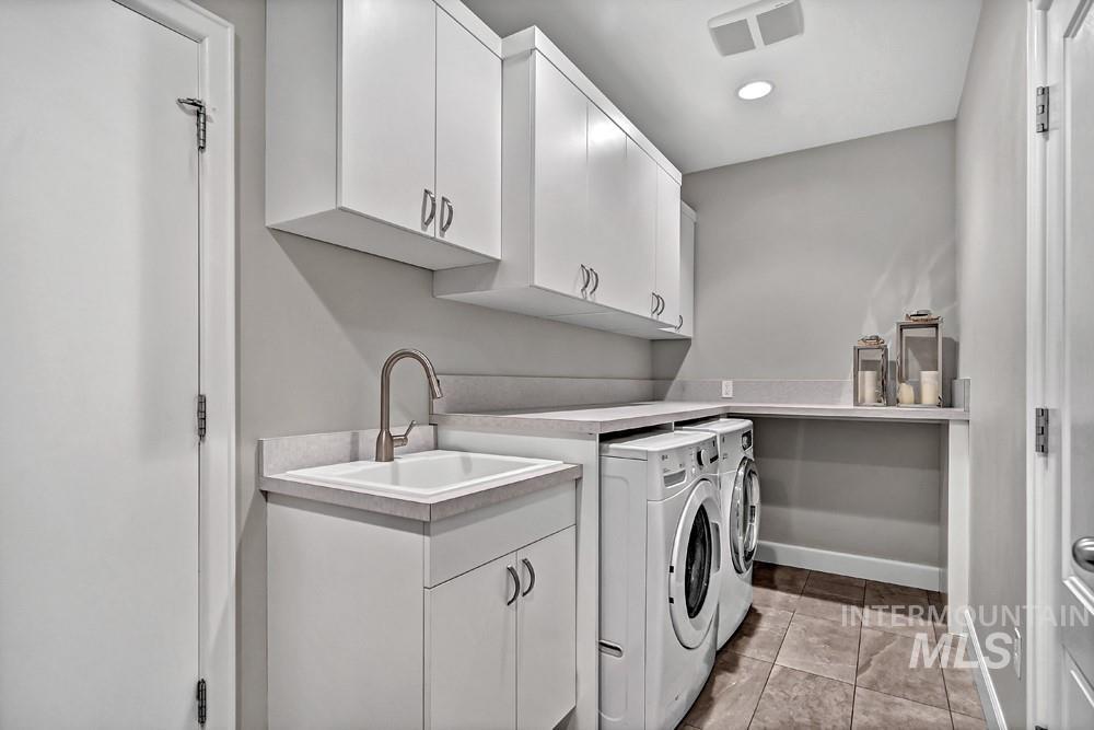 Laundry area with extensive white cabinetry, integrated utility sink with gooseneck faucet, light-toned countertop, and tile flooring