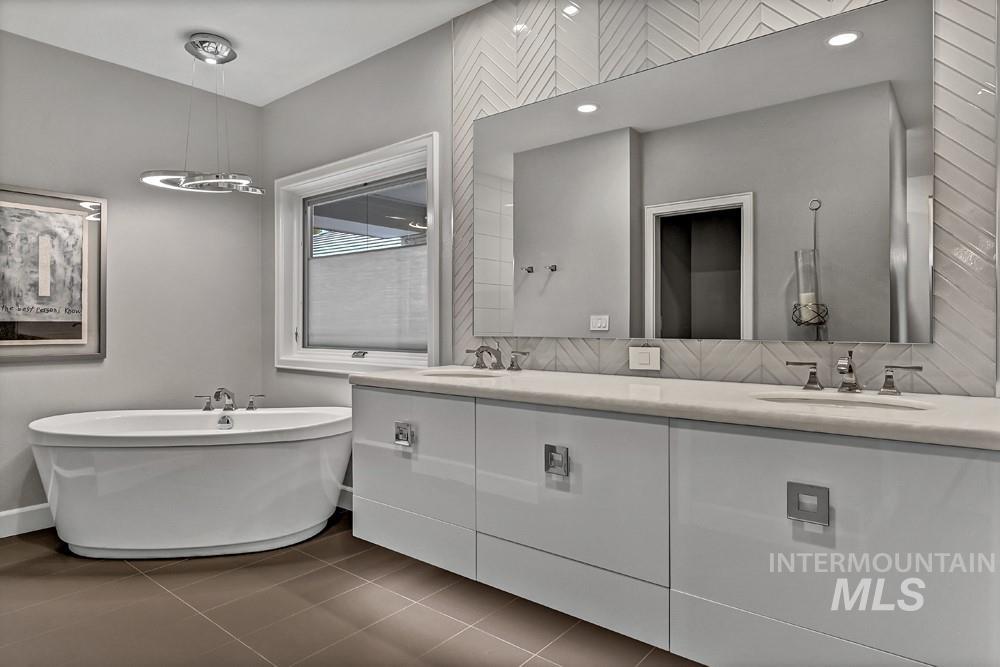 Modern bathroom featuring a freestanding soaking tub, a dual vanity with a light-toned countertop, a large wall-mounted mirror, and tile flooring