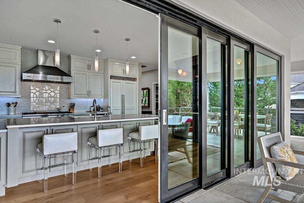 Kitchen featuring a center island with pendant lighting, stainless steel range hood, integrated refrigerator, and light wood-finish flooring