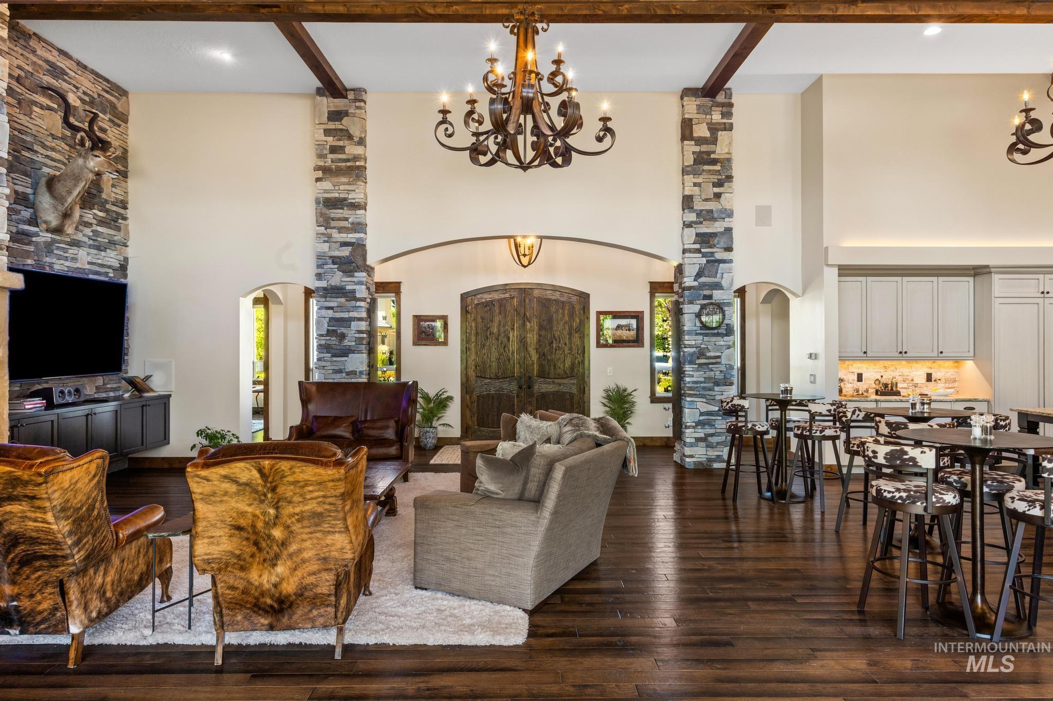 Living room featuring arched walkways, a chandelier, a towering ceiling, dark wood-style floors, and beam ceiling