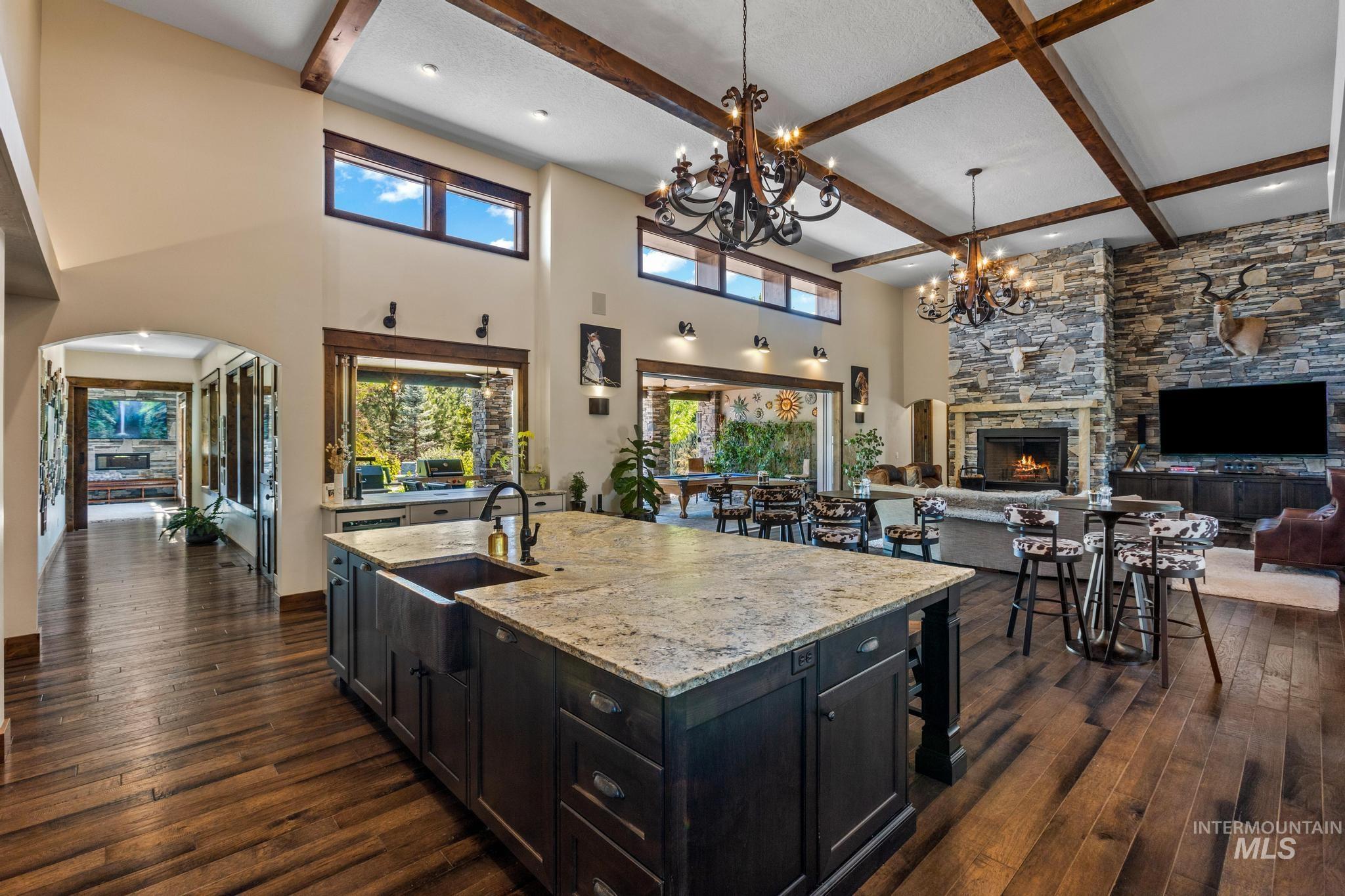 Kitchen featuring dark cabinets, a chandelier, dark wood-style flooring, beamed ceiling, and a stone fireplace