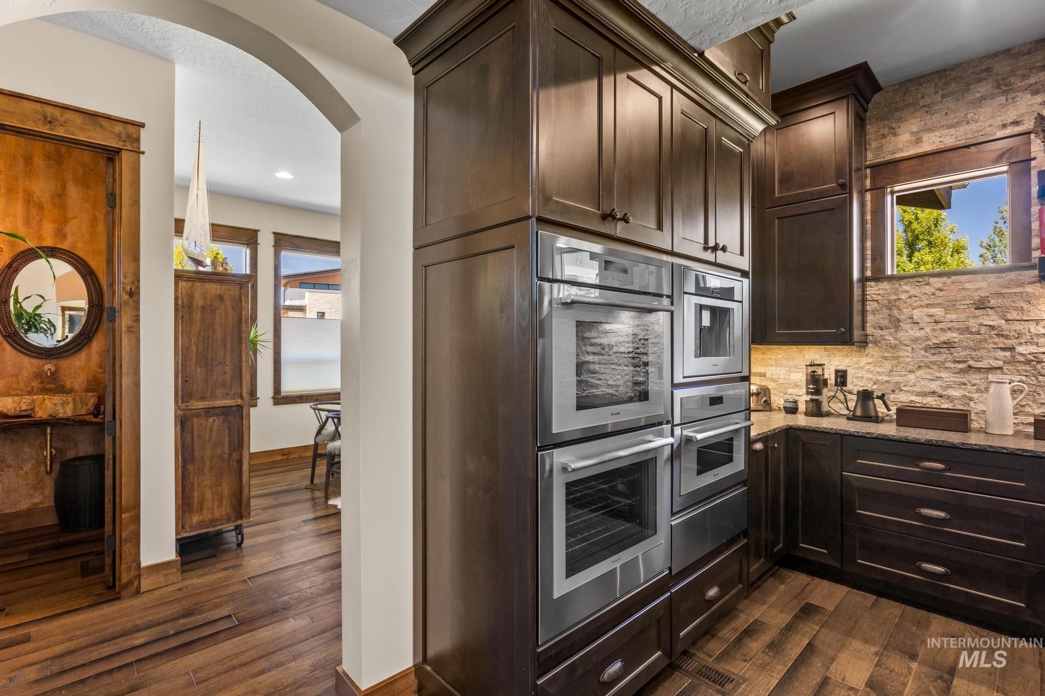 Kitchen with dark wood-type flooring, light stone counters, arched walkways, double oven, and recessed lighting