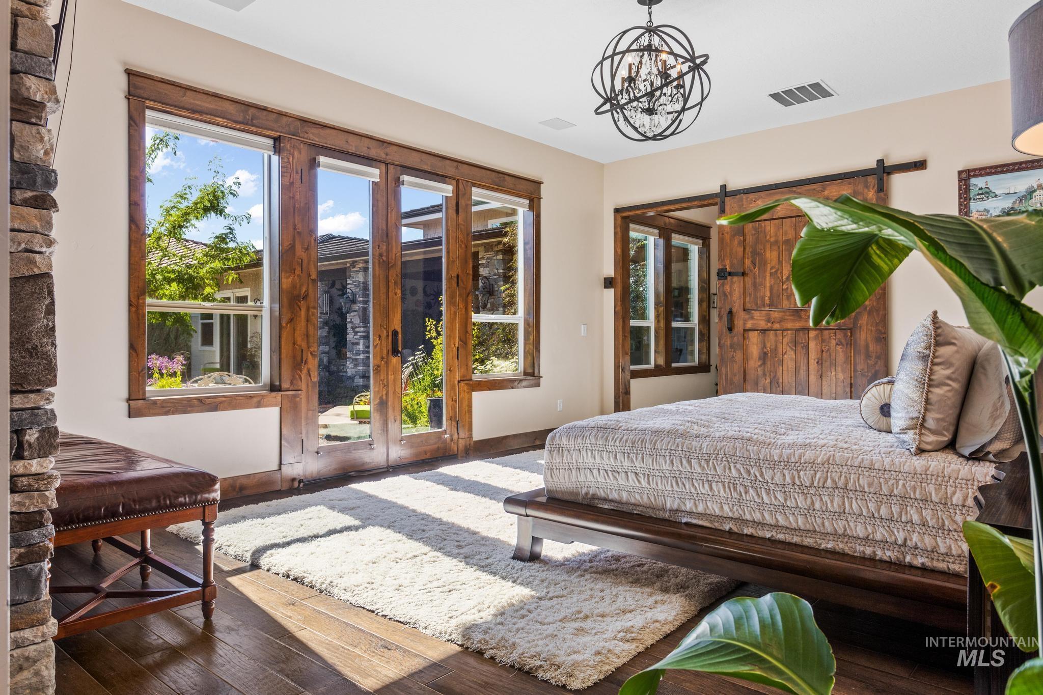 Bedroom featuring access to exterior, wood-type flooring, a barn door, a chandelier, and french doors