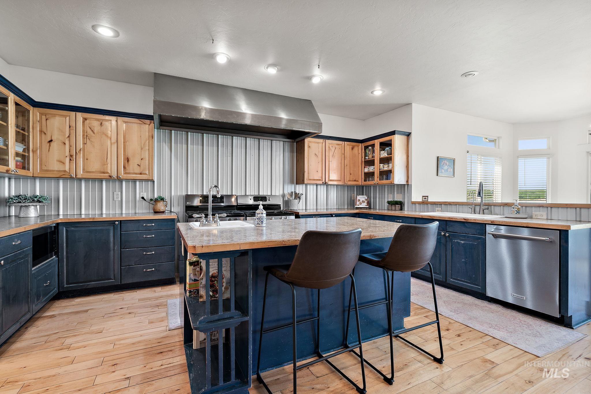 Kitchen with a kitchen breakfast bar, a kitchen island, light wood-style flooring, stainless steel appliances, and glass insert cabinets