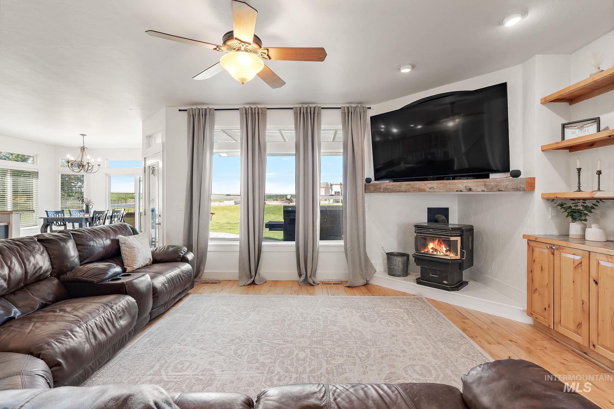 Living room featuring light wood-style flooring, a chandelier, a wood stove, and ceiling fan