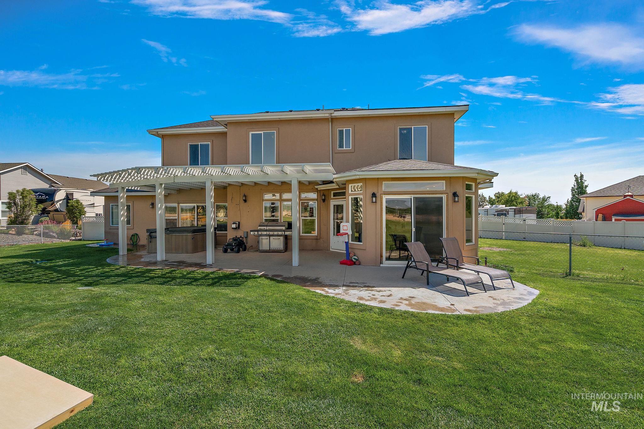 Rear view of house featuring a pergola, stucco siding, a patio, and a hot tub