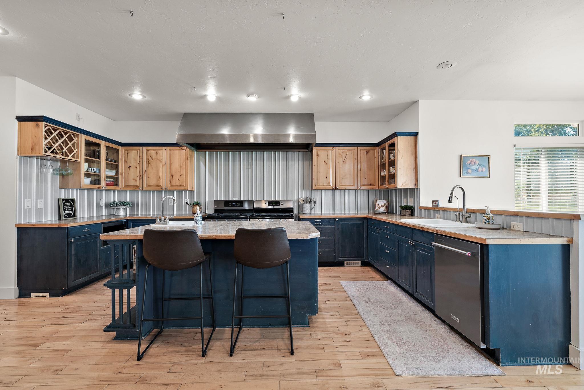 Kitchen featuring a center island with sink, a breakfast bar area, light wood finished floors, appliances with stainless steel finishes, and wall chimney exhaust hood
