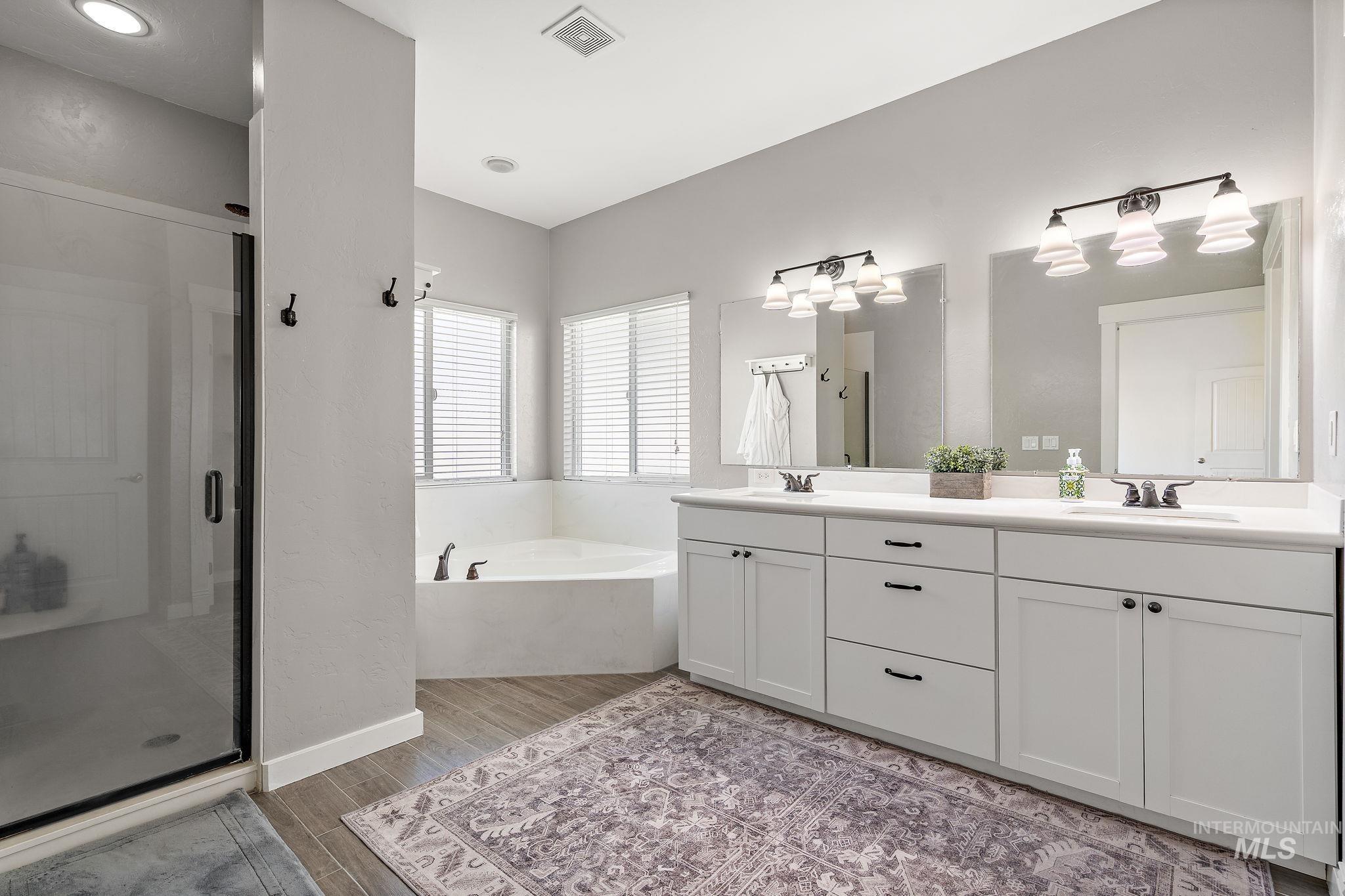 Full bath featuring a stall shower, double vanity, a bath, and wood finished floors