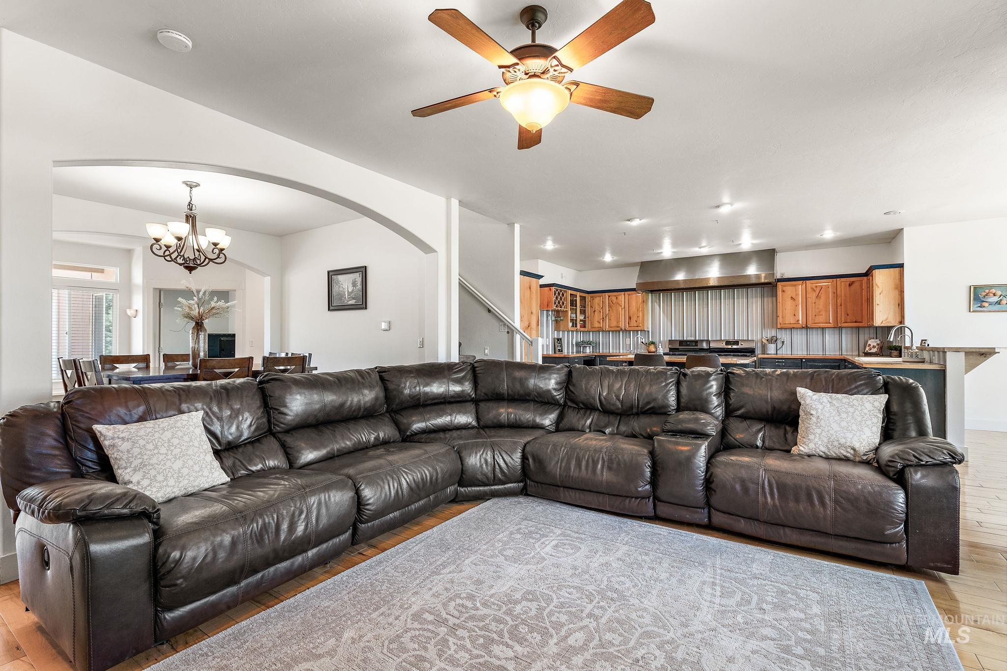 Living area featuring arched walkways, a chandelier, light wood-style flooring, and ceiling fan