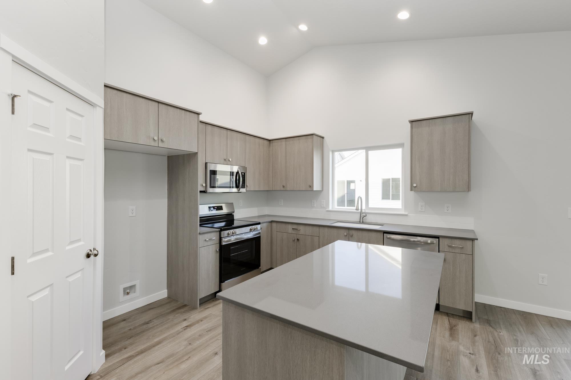 Kitchen featuring light brown cabinets, appliances with stainless steel finishes, modern cabinets, high vaulted ceiling, and a kitchen island