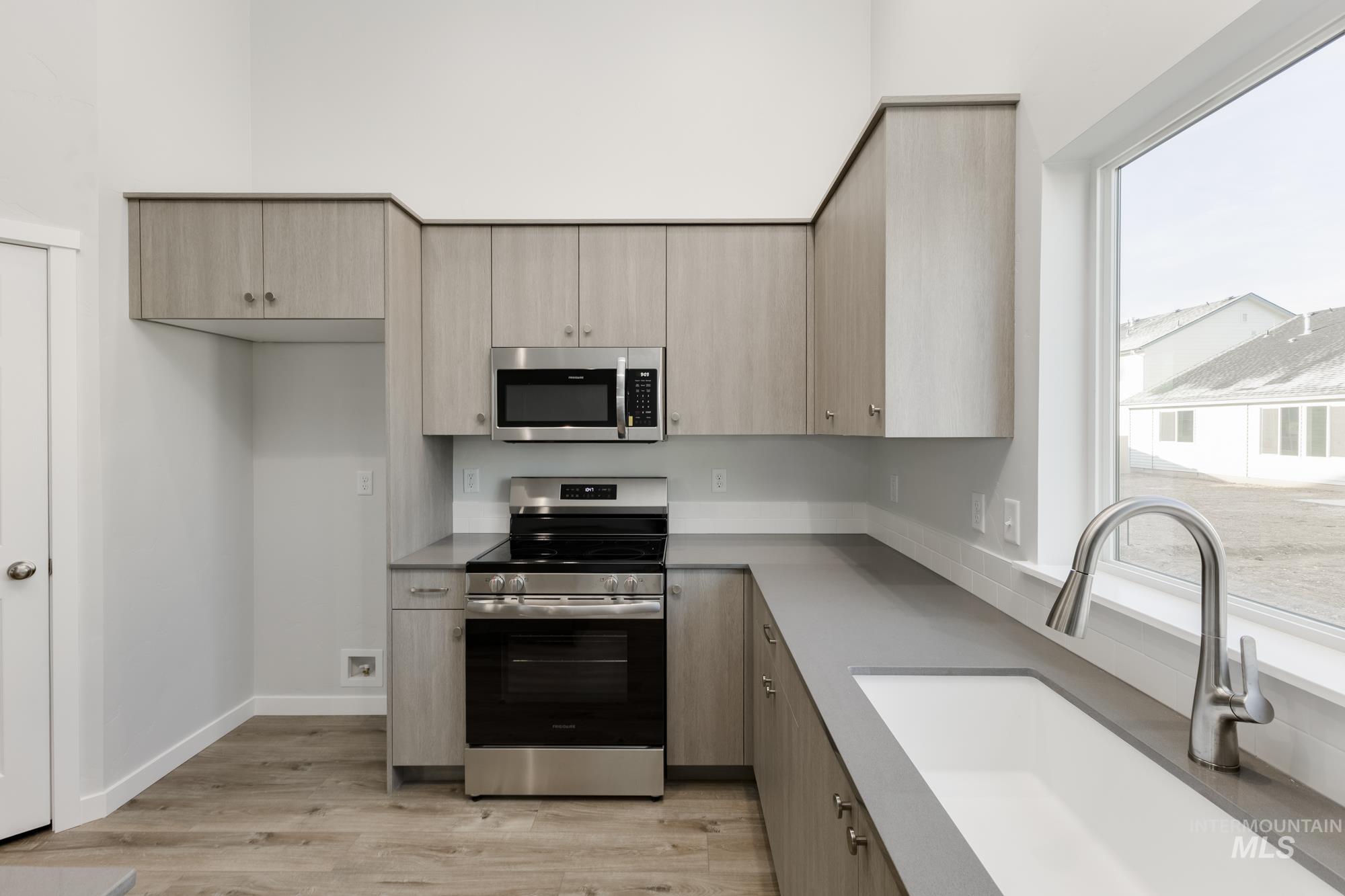 Kitchen with stainless steel appliances, light brown cabinetry, light wood-style floors, and modern cabinets