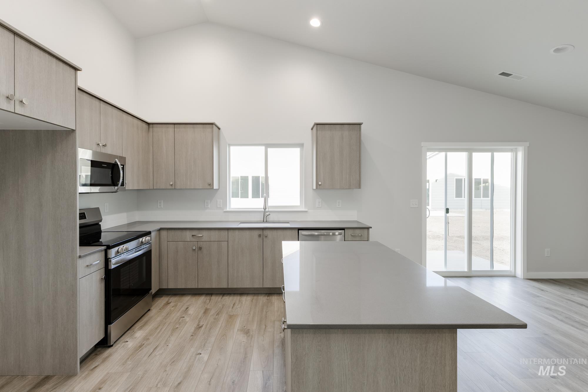 Kitchen featuring light brown cabinetry, stainless steel appliances, vaulted ceiling, light wood-style floors, and modern cabinets