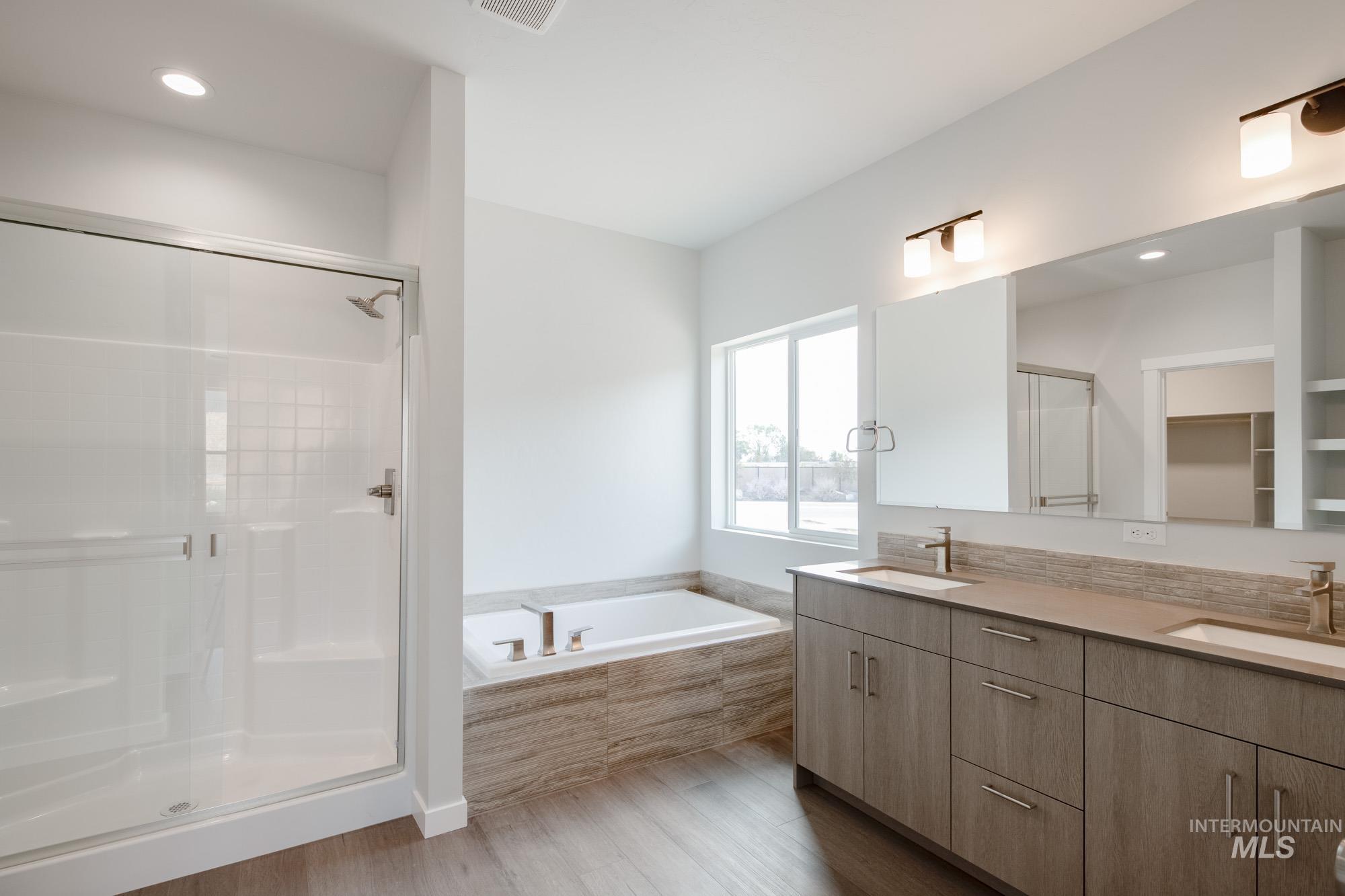 Full bathroom featuring wood finished floors, double vanity, a stall shower, a bath, and recessed lighting