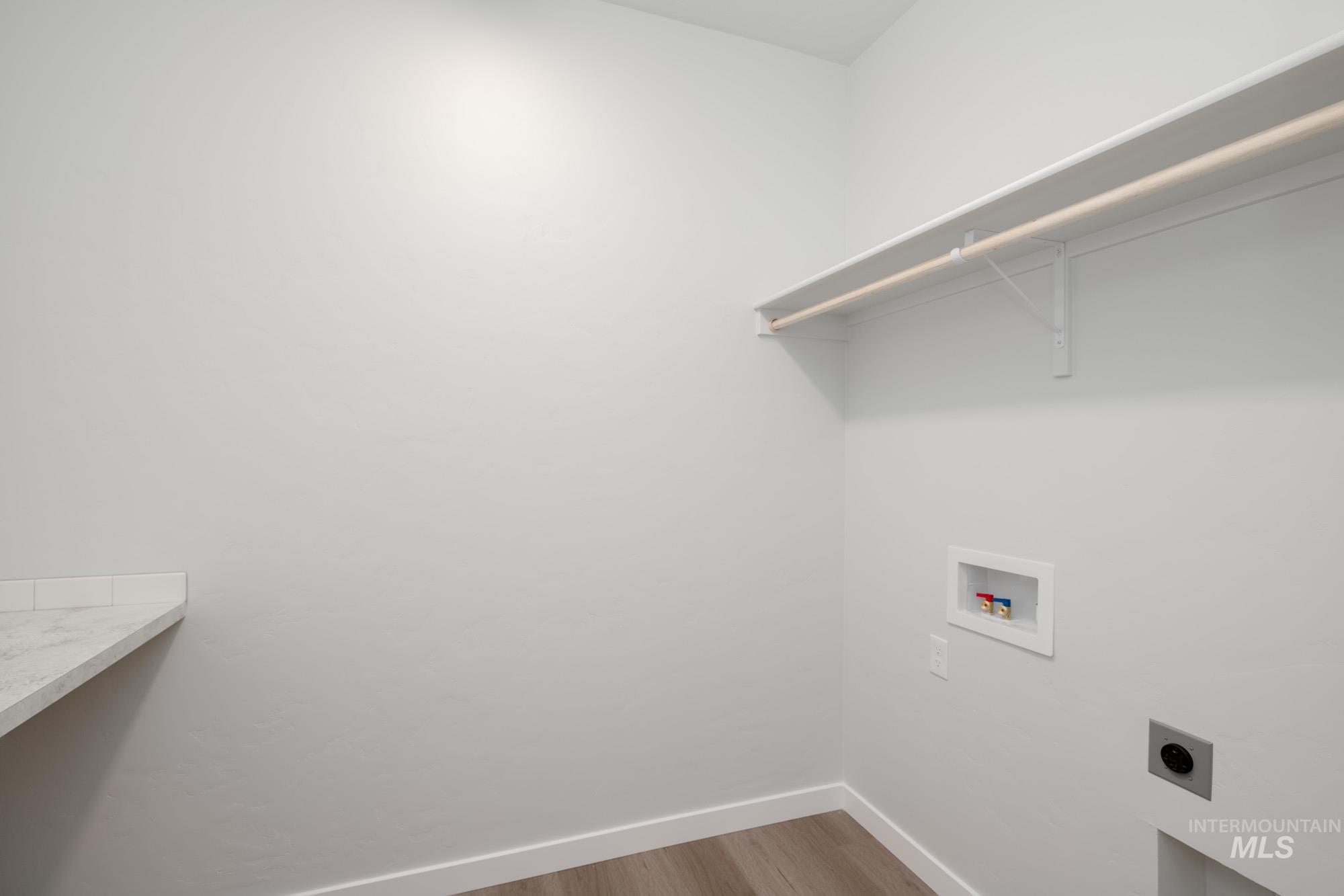 Washroom with electric dryer hookup, hookup for a washing machine, and wood finished floors