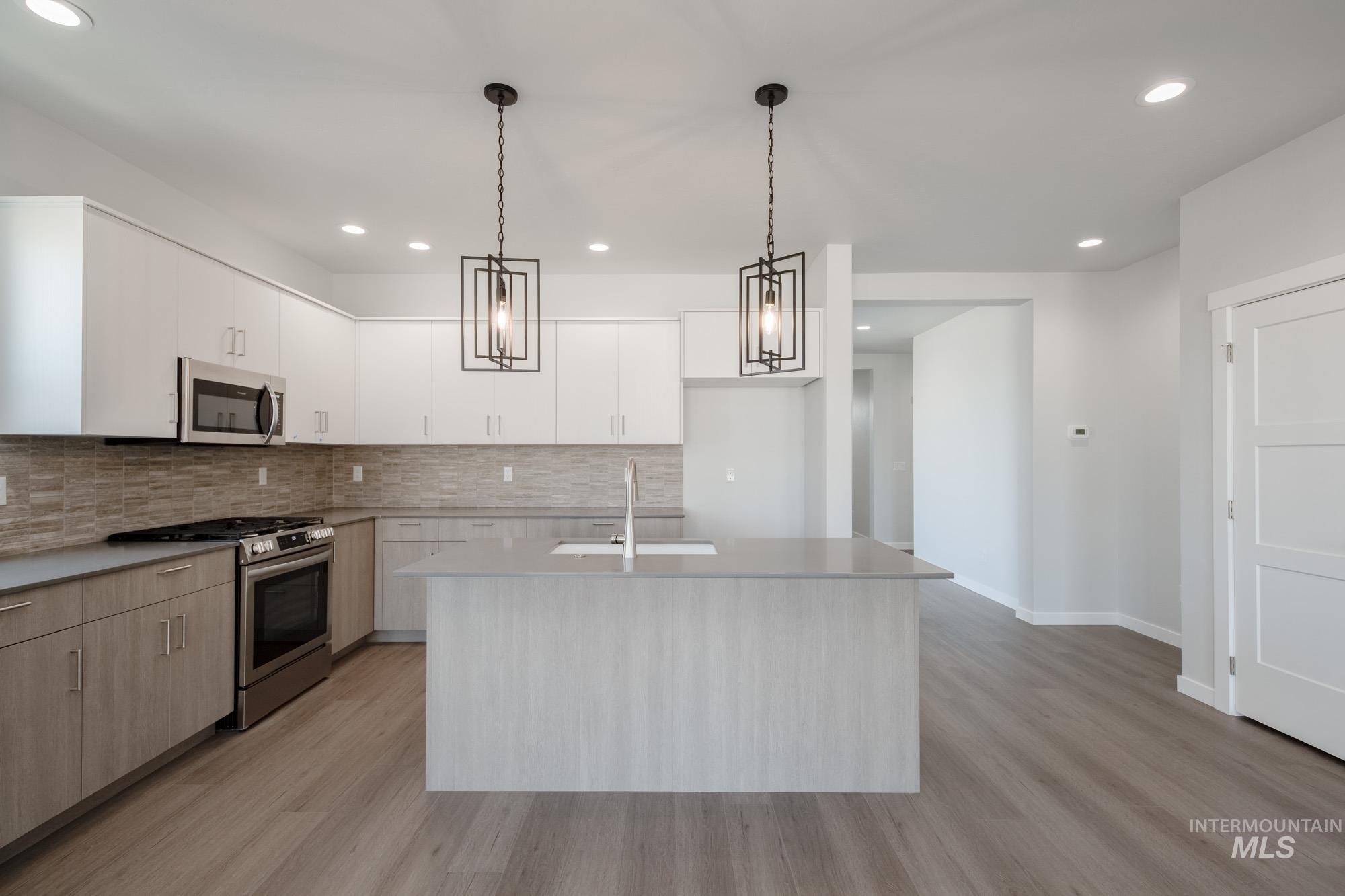 Kitchen featuring appliances with stainless steel finishes, recessed lighting, light wood-style flooring, light countertops, and an island with sink