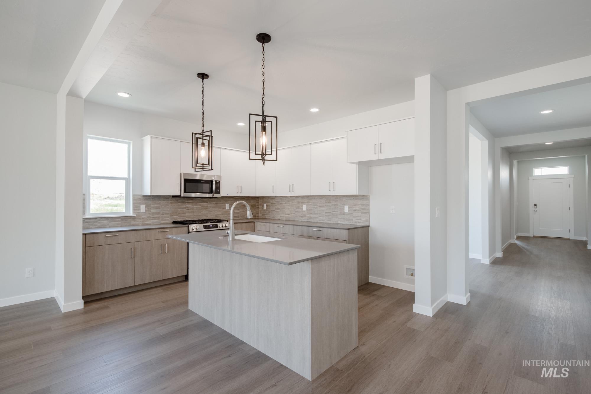 Kitchen featuring decorative backsplash, stainless steel microwave, light wood-style floors, an island with sink, and recessed lighting