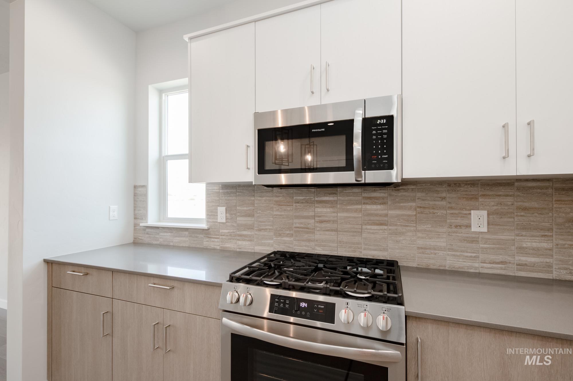 Kitchen featuring stainless steel appliances, light countertops, backsplash, and white cabinetry