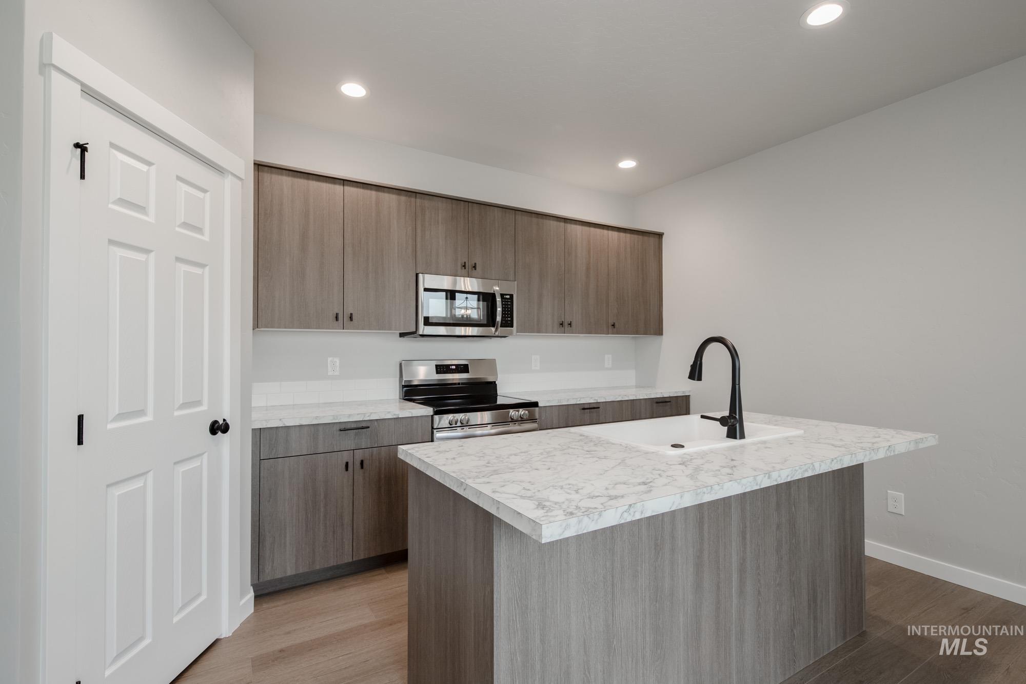 Kitchen with light countertops, stainless steel appliances, light wood-style floors, an island with sink, and recessed lighting
