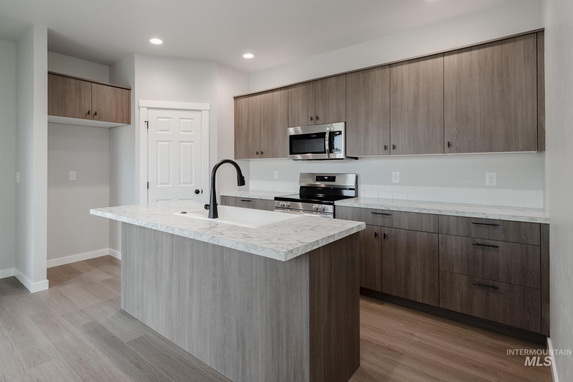 Kitchen featuring light countertops, an island with sink, stainless steel appliances, light wood-style flooring, and recessed lighting