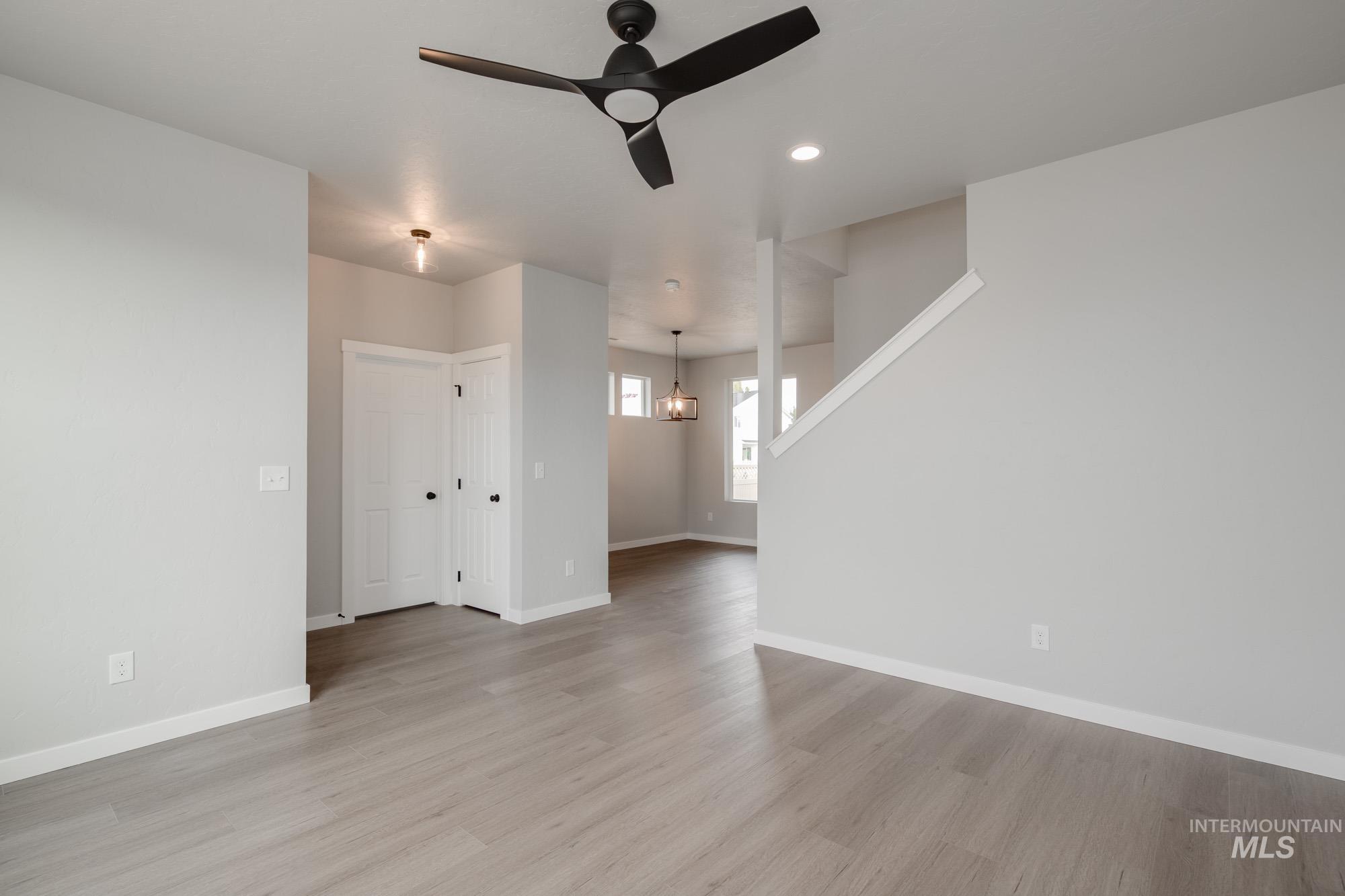 Unfurnished living room with light wood finished floors, ceiling fan, recessed lighting, stairs, and a chandelier