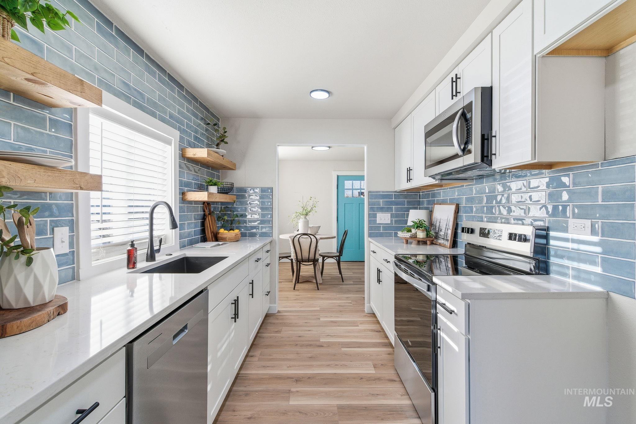 Kitchen with appliances with stainless steel finishes, white cabinets, light stone counters, and light wood-type flooring