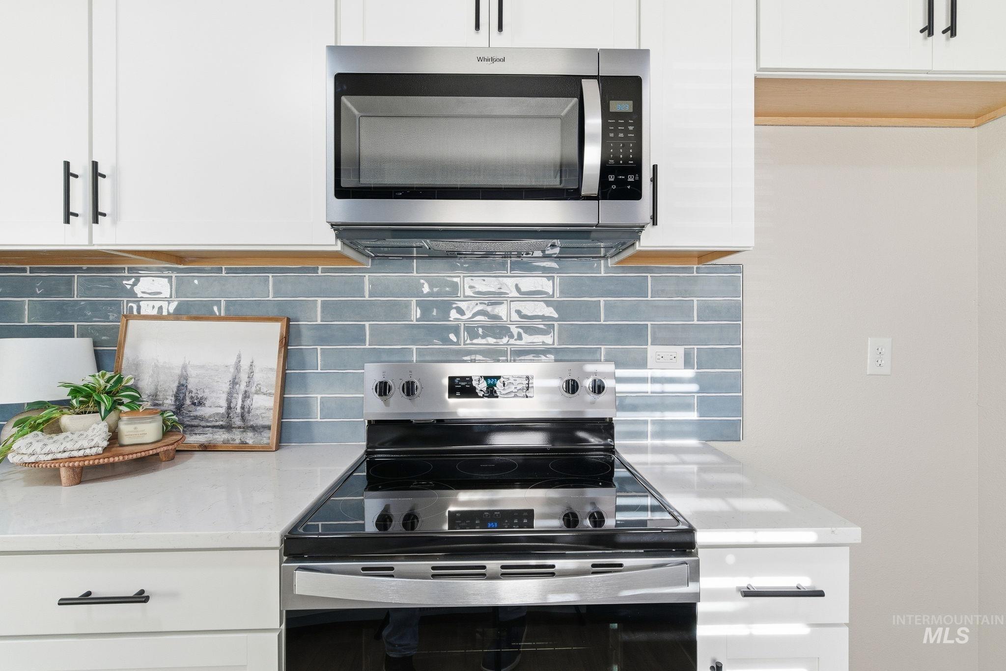 Kitchen with appliances with stainless steel finishes, white cabinets, backsplash, and light stone countertops