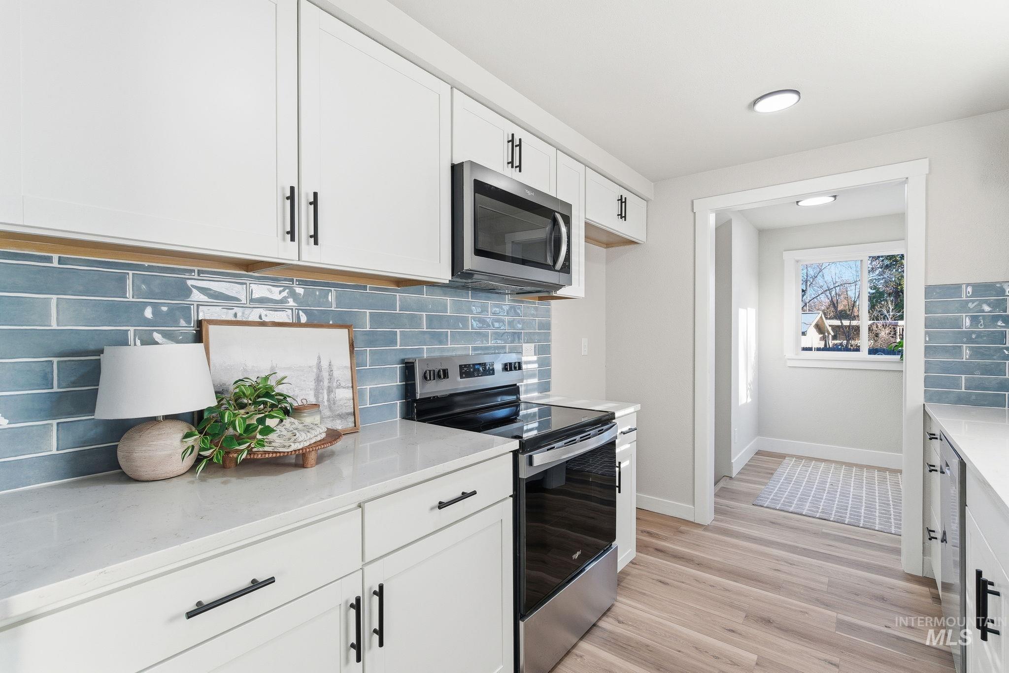 Kitchen featuring stainless steel appliances, backsplash, white cabinetry, light wood-style floors, and light stone countertops