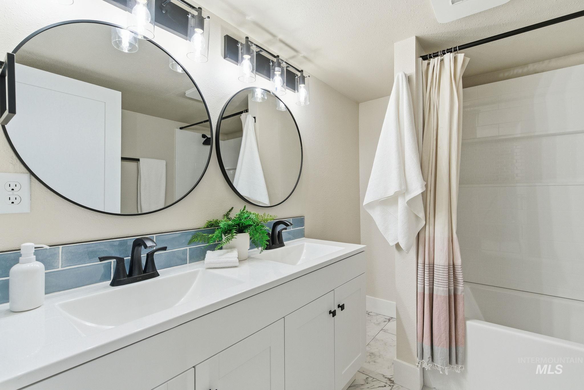 Bathroom with double vanity, shower / bath combo with shower curtain, and light marble finish flooring