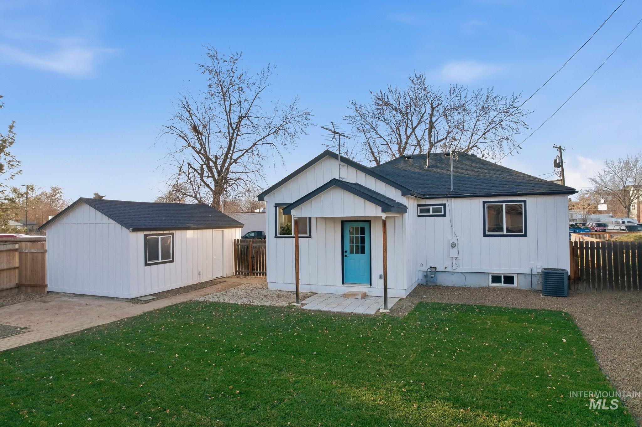 Back of house featuring a shingled roof, an outdoor structure, a fenced backyard, a patio area, and board and batten siding